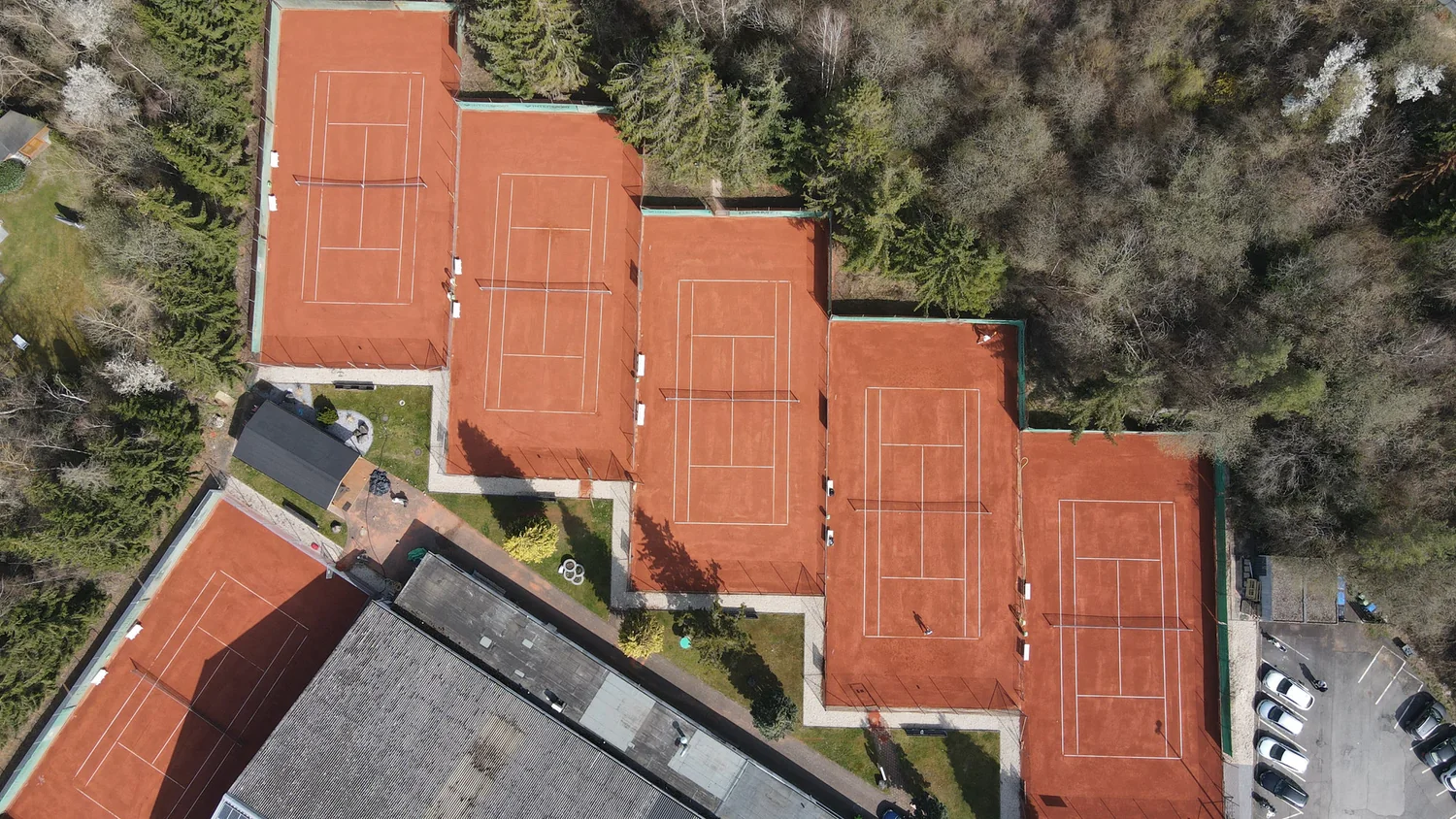 Luftbild der Anlage des TC Grün-Weiß Elz: sechs rote Sandplätze, das Clubhaus und der angrenzende Wald.